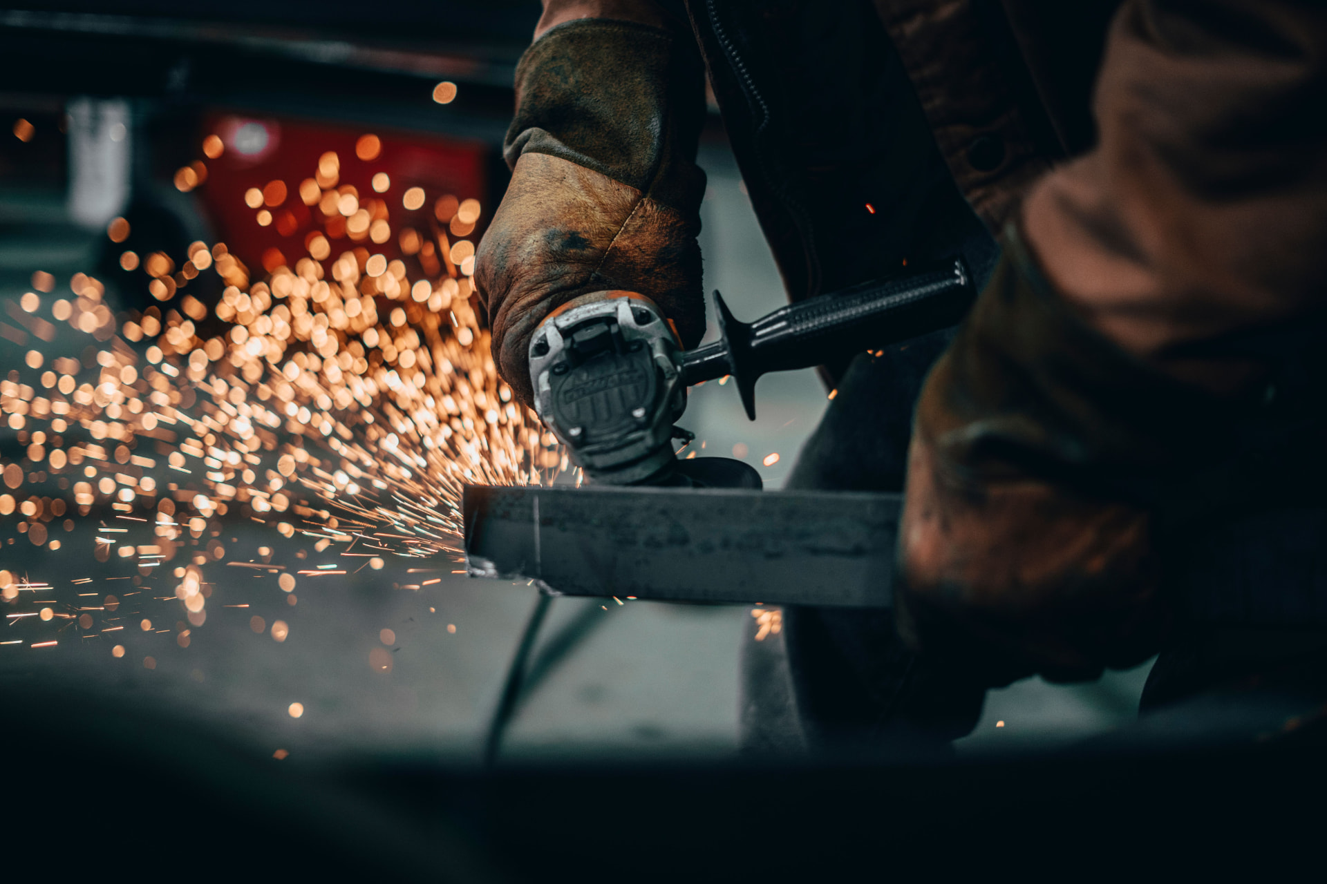 Steel fabricator cutting a steel section with an angle grinder, sparks flying